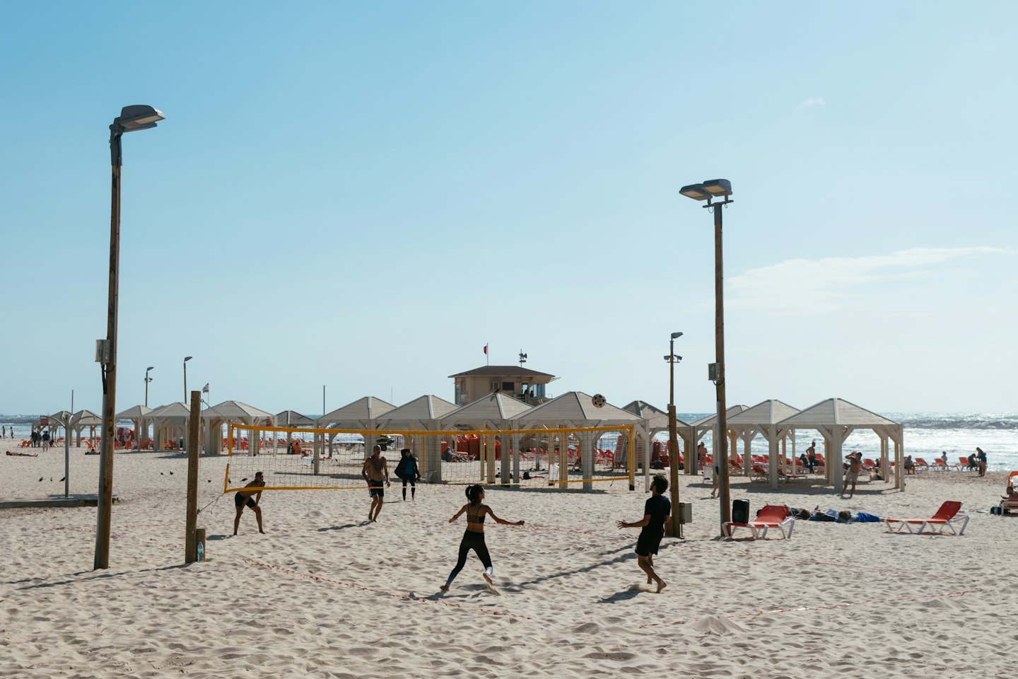Persone che giocano a beach volley in una giornata di sole con l'oceano sullo sfondo.
