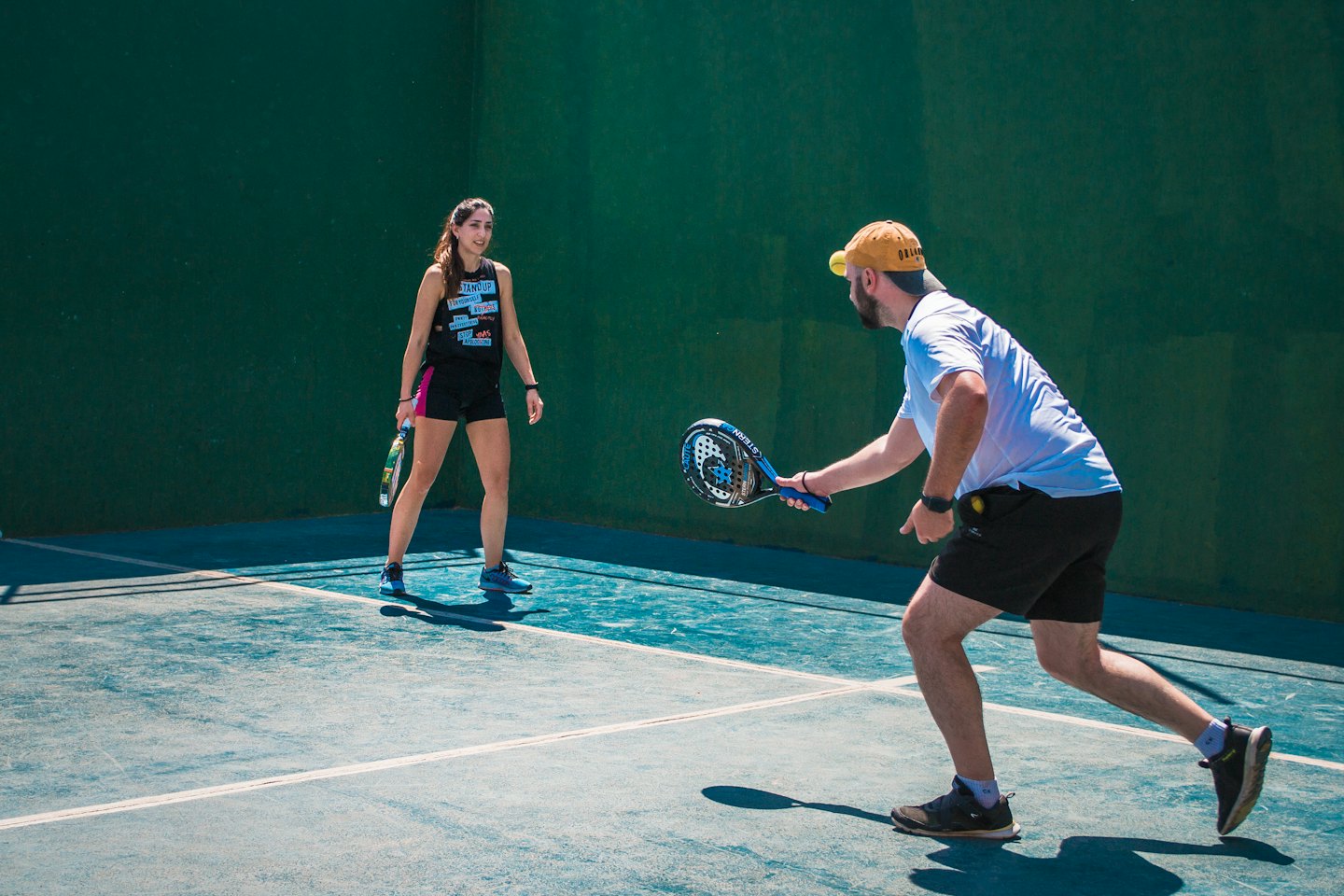 Uomo e donna giocano a padel su un campo all'aperto.